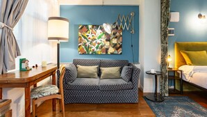 A cozy room with a sofa, a dining table with chairs, a lamp, a painting on the wall, and a bed with a yellow headboard.