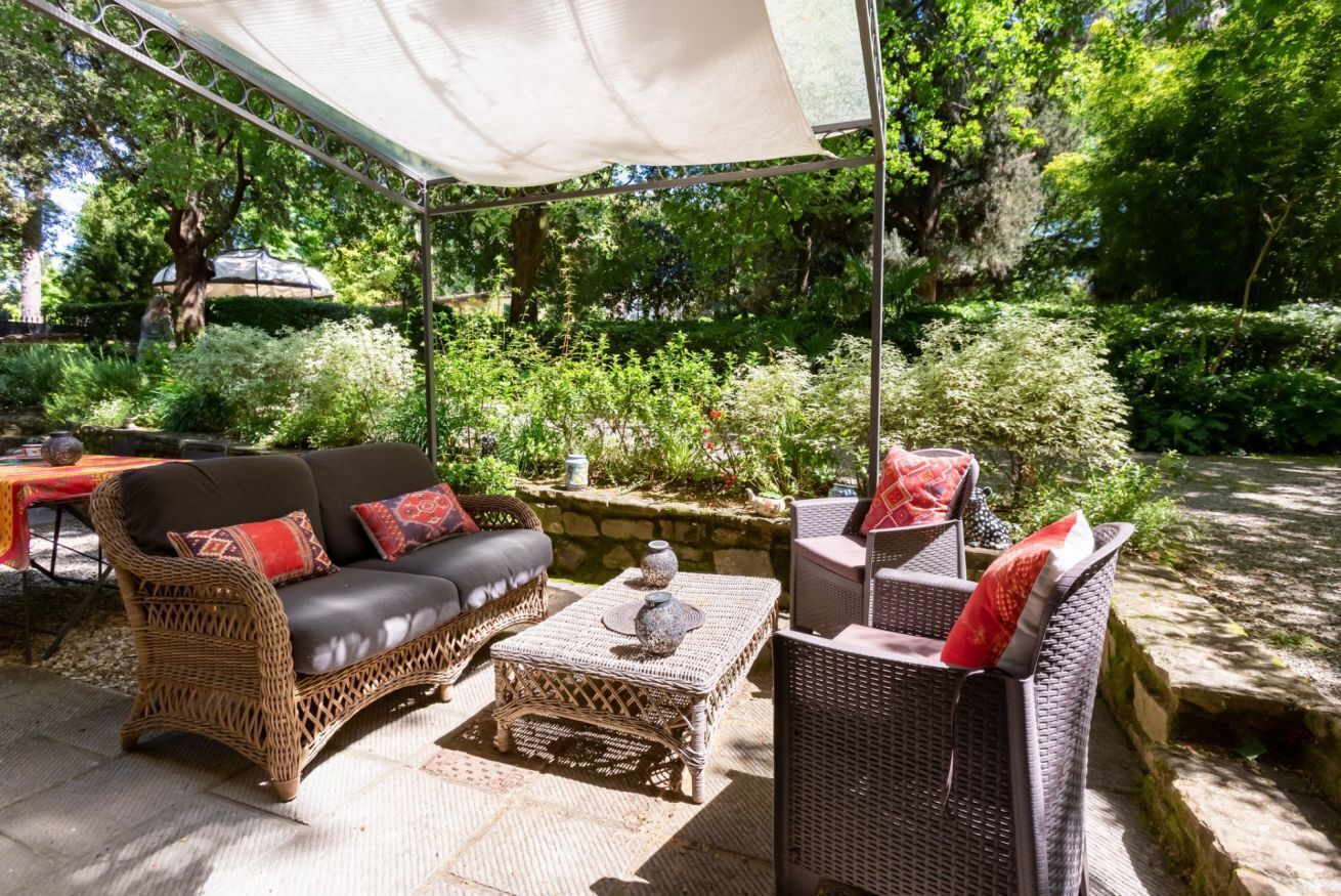Un patio exterior con mobiliario de mimbre, una mesa y una silla colgante.