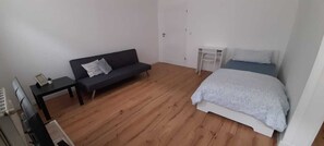 A small, furnished room with a sofa, a bed, a small table, and a white door. - Nice apartment close to Leipzig (Zeitz)
