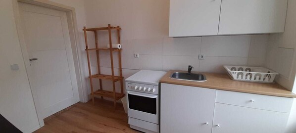 A small kitchen with a stove, oven, sink, and wooden shelves. - Nice apartment close to Leipzig (Zeitz)