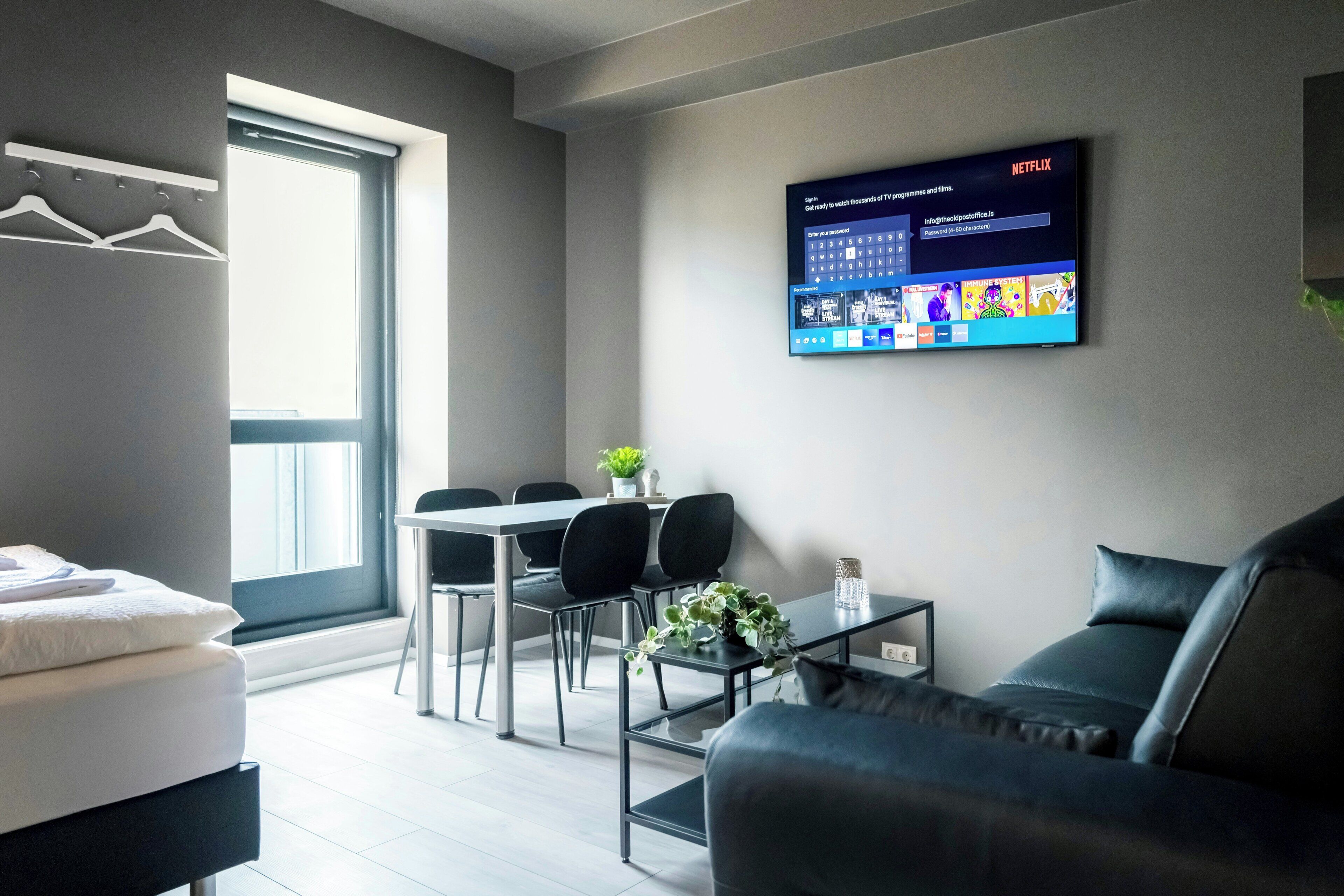 Ein modernes Wohnzimmer mit einem an der Wand befestigten Flachbildfernseher, einem Essbereich mit Tisch und Stühlen sowie einem Sofa.