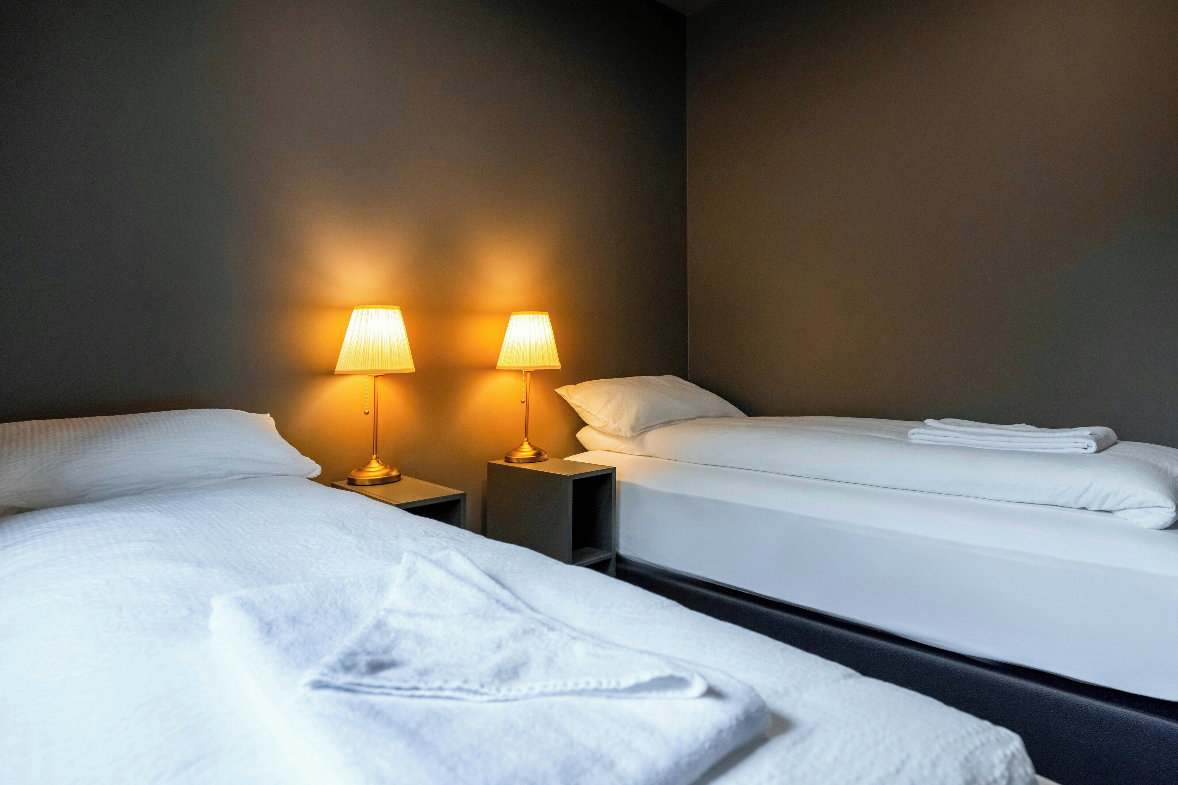 Een hotelkamer met twee bedden, elk voorzien van witte lakens en kussens, en twee nachtlampjes.