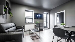 A modern living room with a black leather sofa, a glass-top coffee table, and a dining area with a rectangular table and black chairs. - The New Post Office (Vestmannaeyjar)