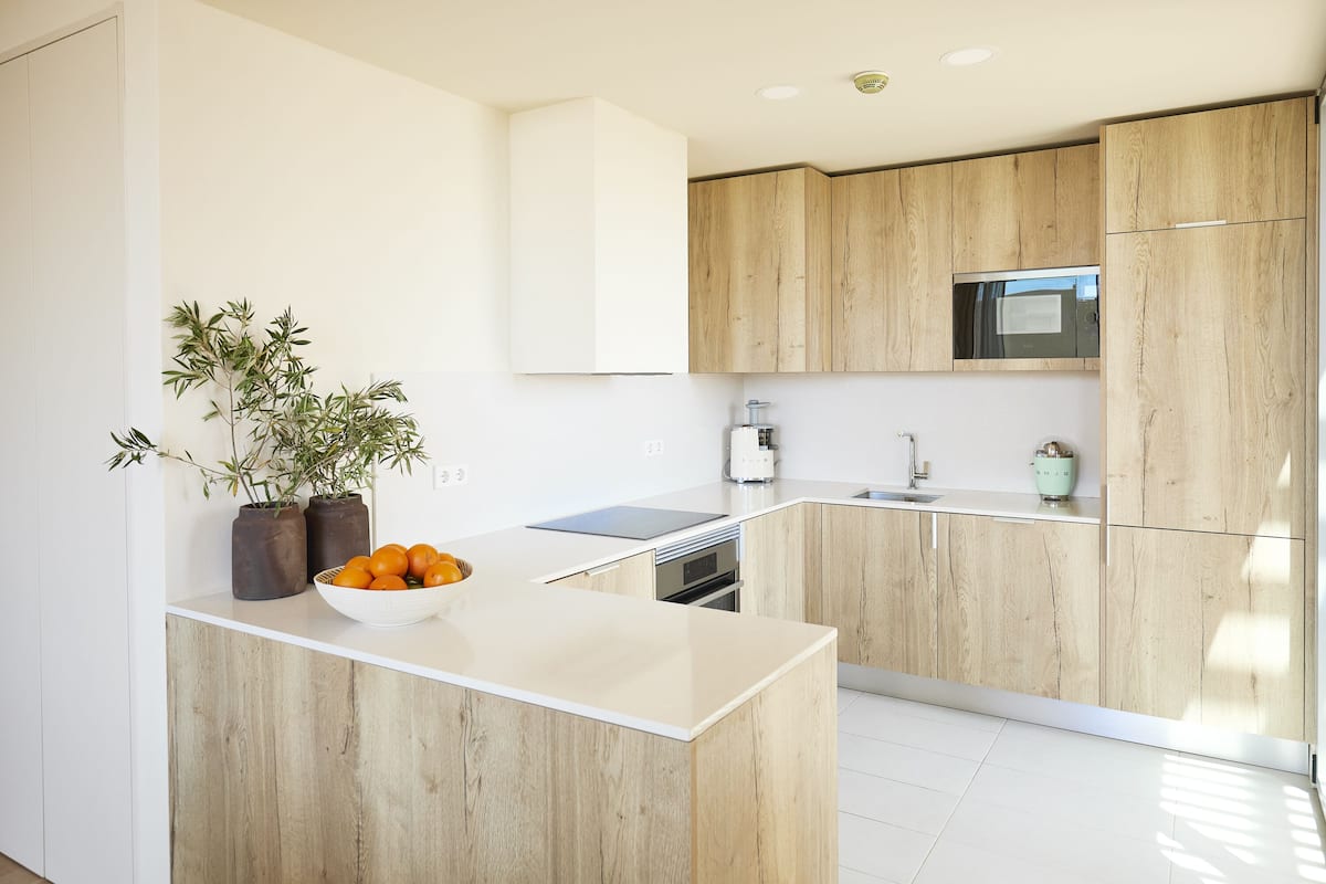 Une cuisine moderne avec des meubles en bois, un plan de travail blanc et un saladier rempli d’oranges.