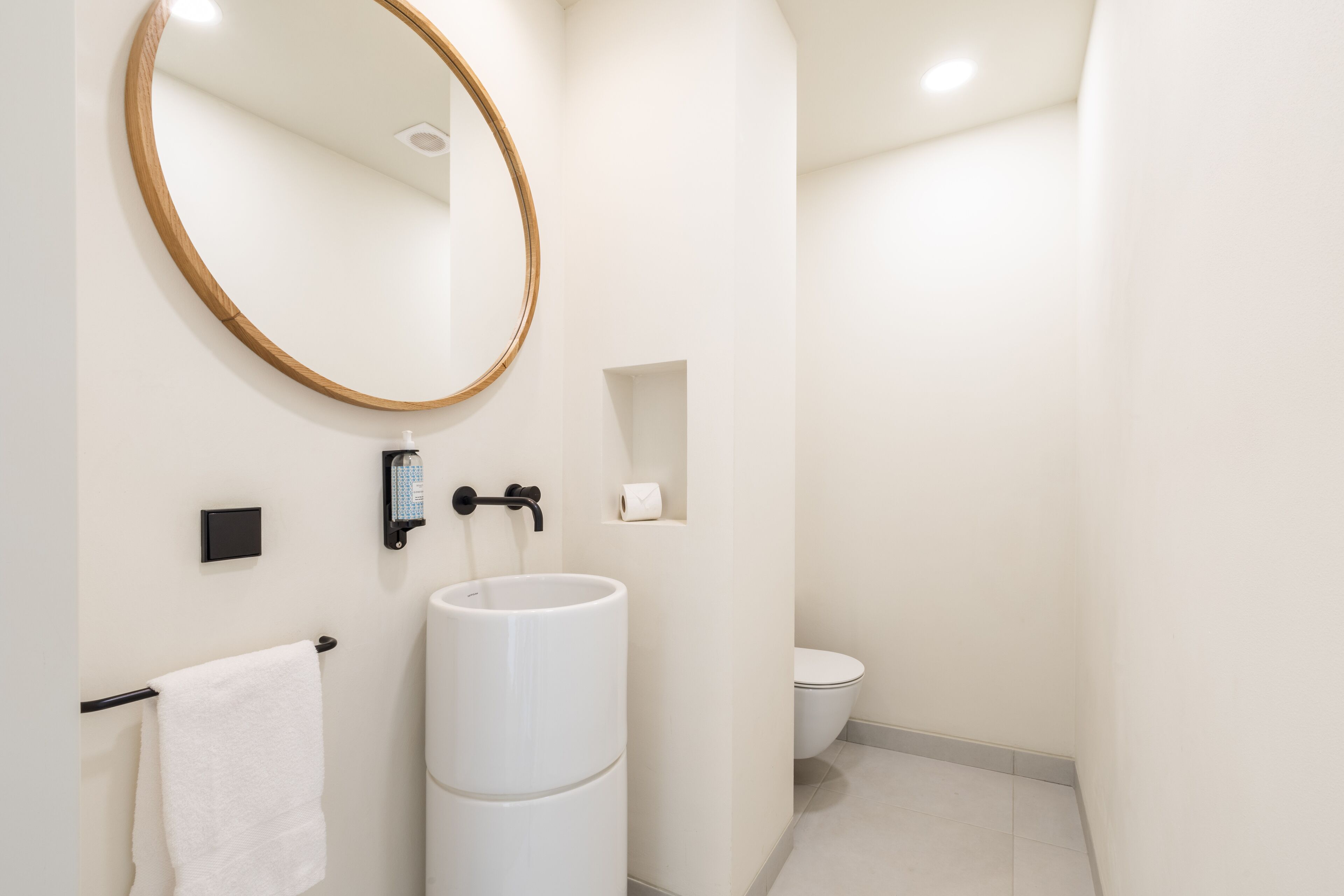 Een moderne badkamer met een grote spiegel, een witte wastafel, een handdoekhouder en een toilet.