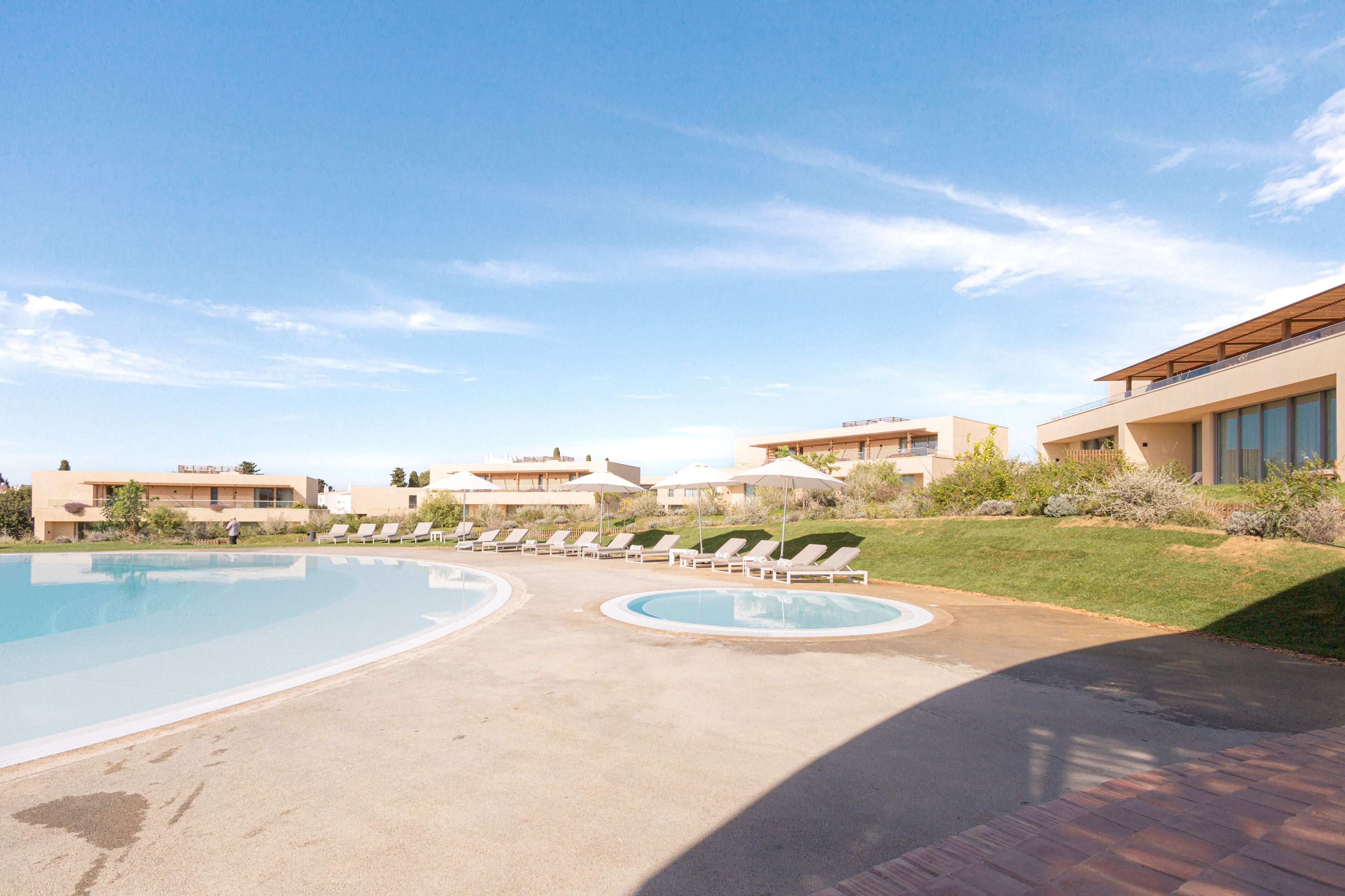 A swimming pool area with lounge chairs and umbrellas, surrounded by modern buildings.