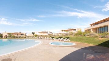 A swimming pool area with lounge chairs and umbrellas, surrounded by modern buildings.
