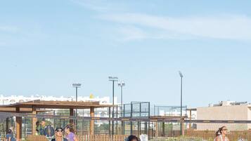 Una cancha de voleibol con jugadores con ropa deportiva, una valla de madera y un cielo despejado.