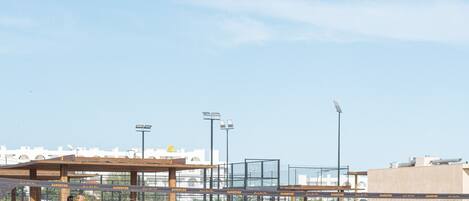 A volleyball court with players in sports attire, a wooden fence, and a clear sky.