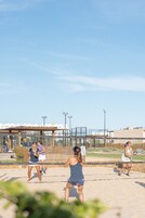 Una cancha de voleibol con jugadores con ropa deportiva, una valla de madera y un cielo despejado.