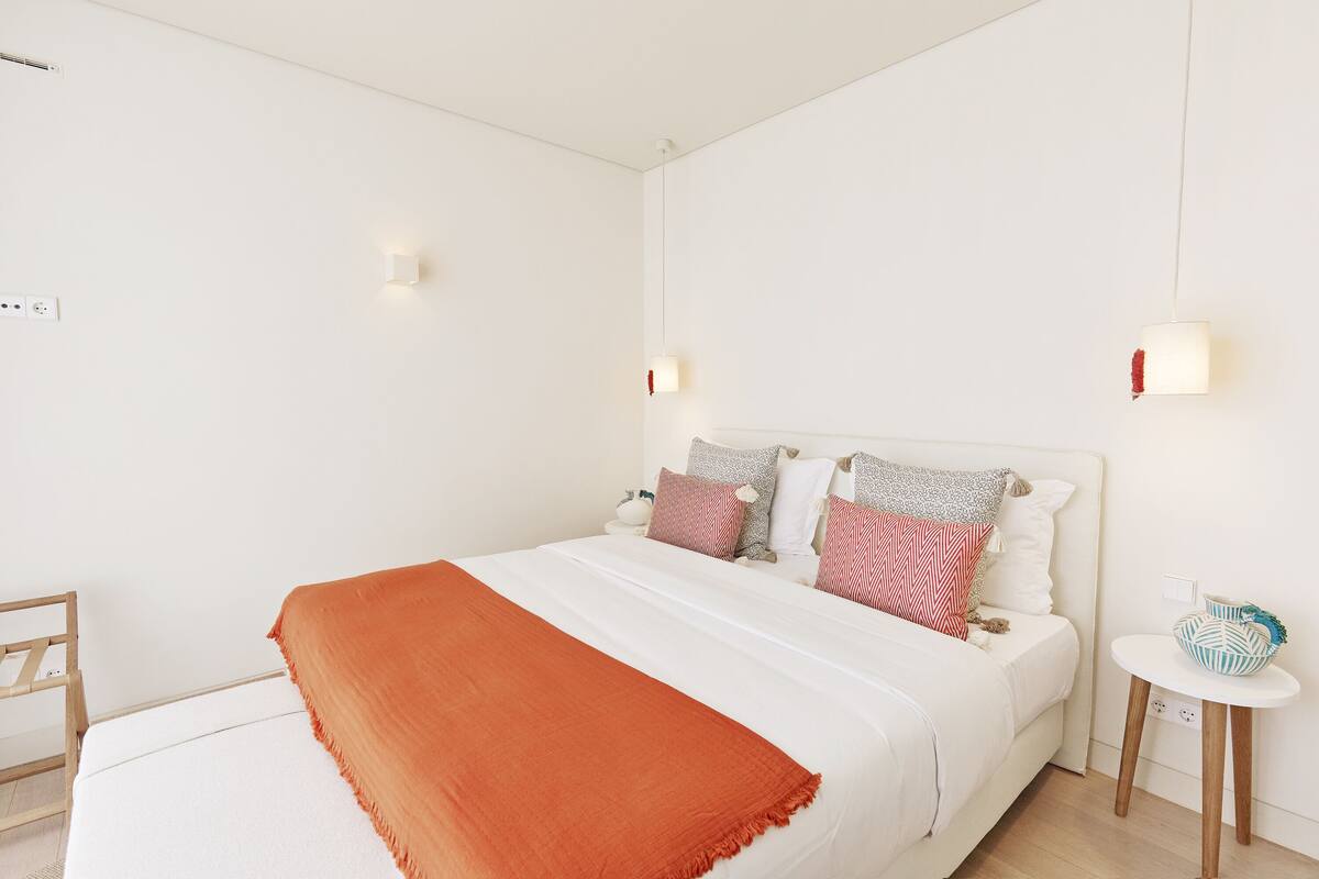 Une chambre à coucher bien rangée, avec un lit, des tables de chevet et une petite table ronde agrémentée d’objets décoratifs.