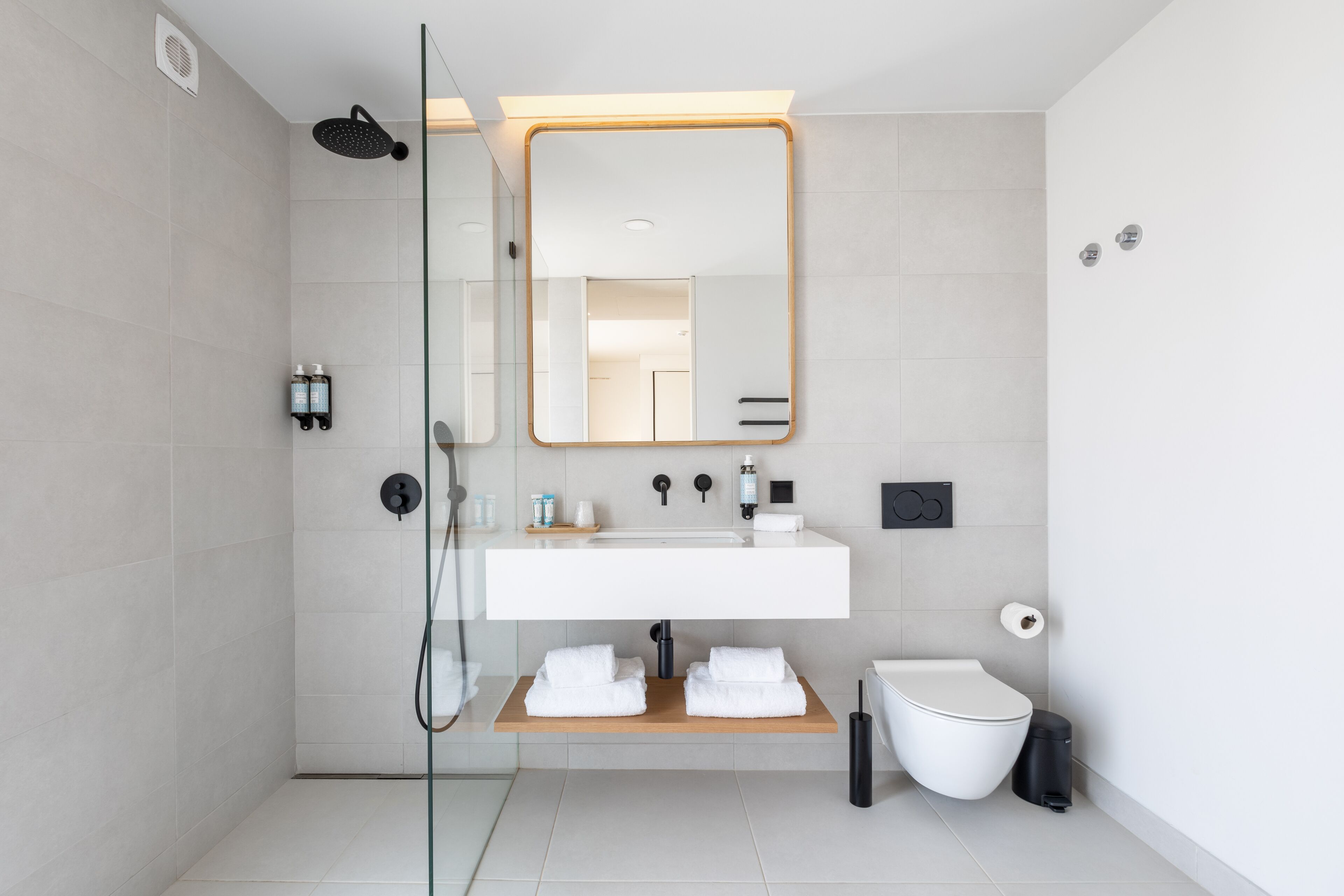 A modern bathroom with a glass-enclosed shower, a large mirror, a white sink, and a toilet.