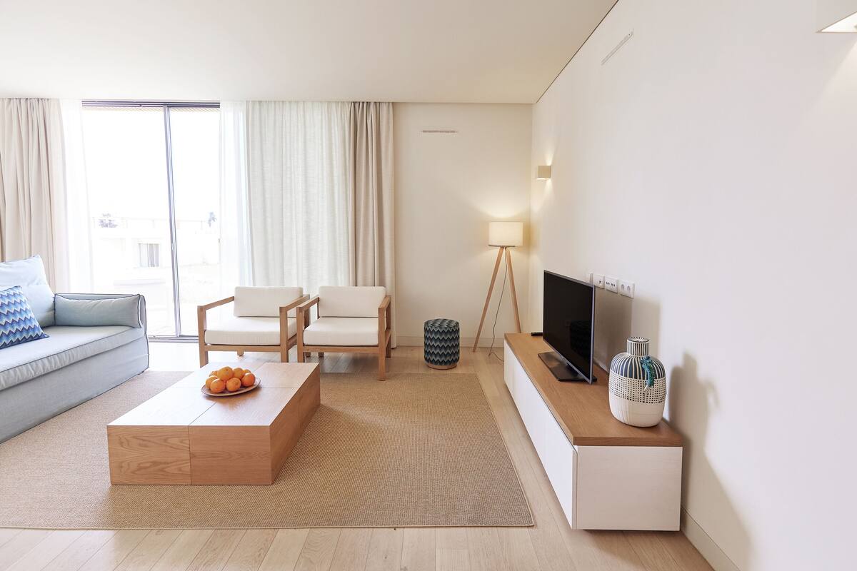 Un salon moderne avec un canapé, une table basse ornée d’oranges, un téléviseur posé sur un meuble et une lampe.