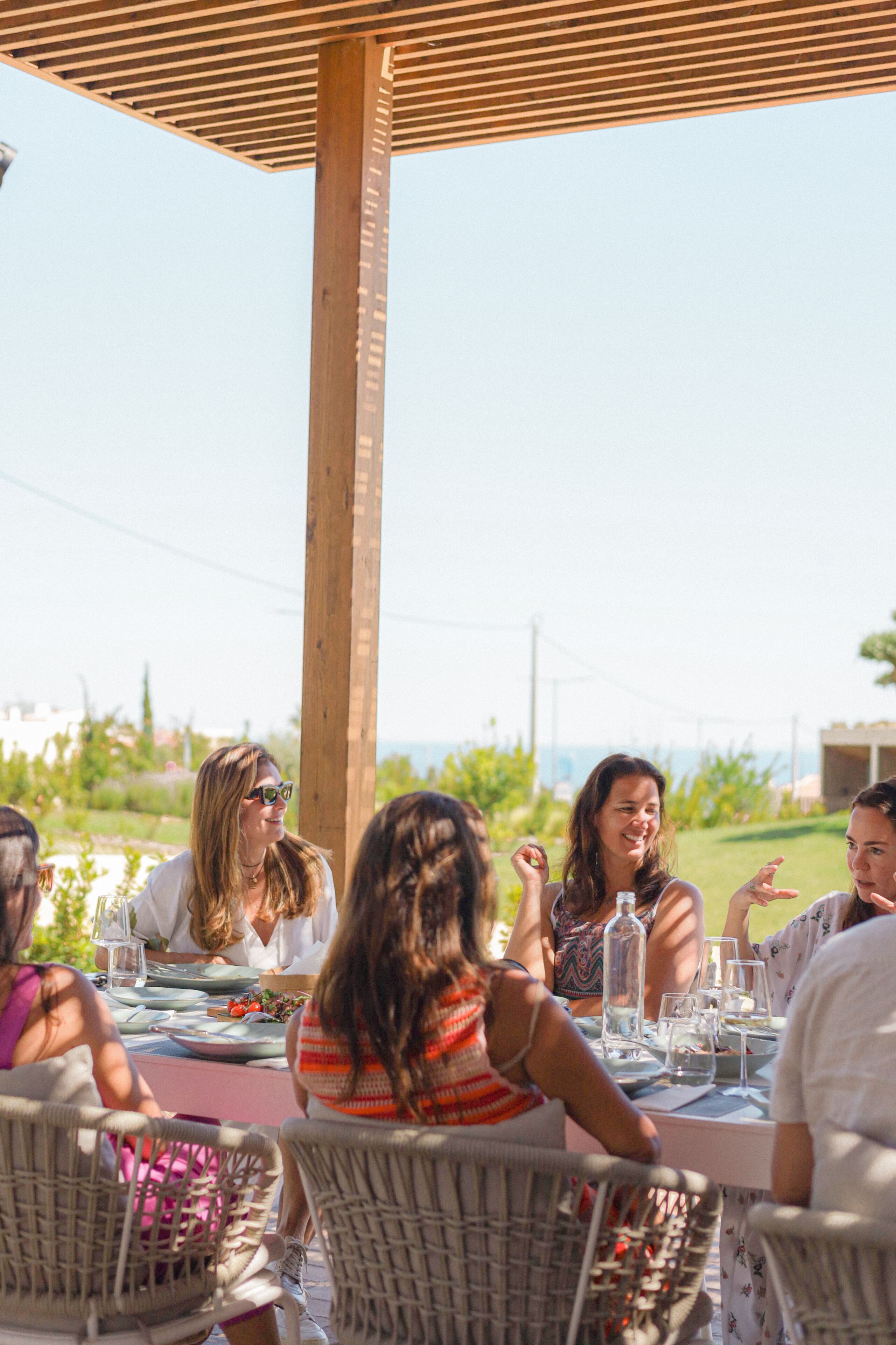 A group of people dining at an outdoor table with a wooden pergola overhead.