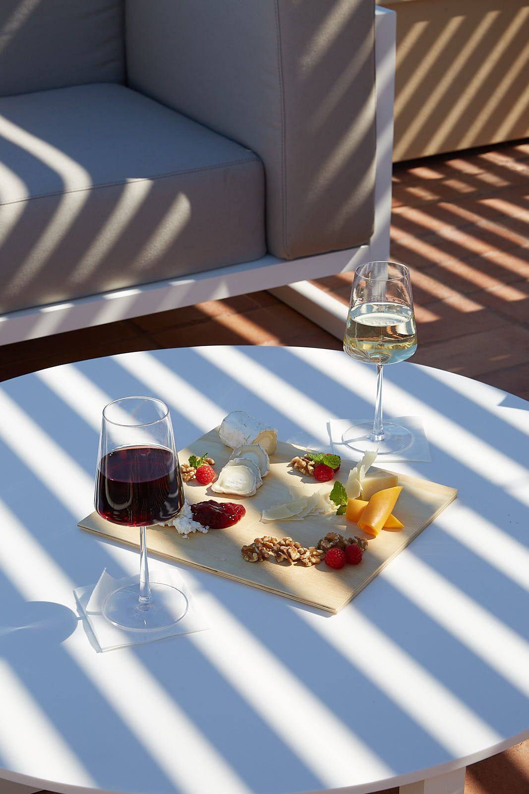 A round table with a white tablecloth, two wine glasses, and a charcuterie board with cheese, fruits, and nuts.