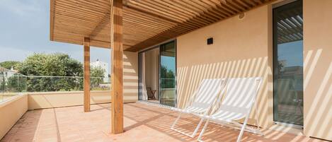 Un espacio al aire libre cubierto con techo de madera, una silla blanca y un vidrio que da a un balcón.
