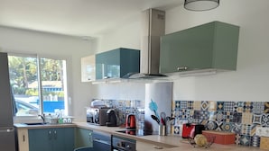 Una cocina moderna con una isla central, sillas azules y vistas al exterior.