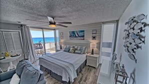 A bedroom with a large bed, a ceiling fan, a view of the ocean, a balcony, and nautical decor.