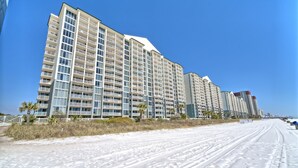 A beachfront hotel with multiple high-rise buildings, sandy beach, and clear blue sky.