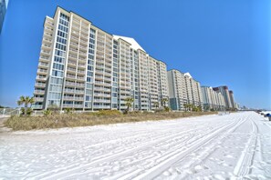 Un hôtel en bord de mer, avec plusieurs étages, des balcons et une plage de sable au premier plan.