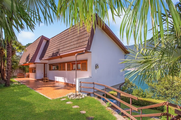 Una casa moderna con techo de tejas, terraza de madera y vista al mar.