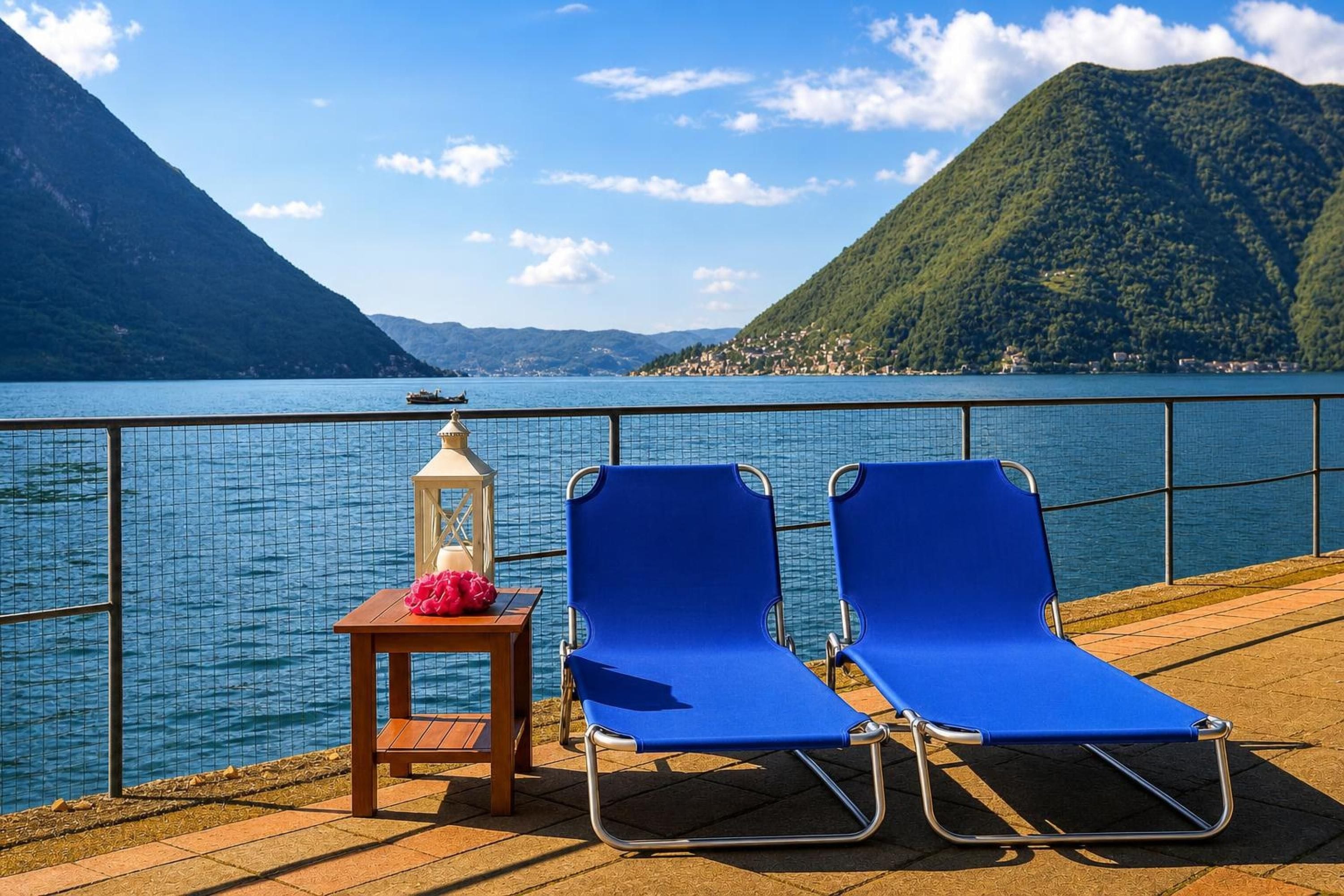 Vista para o lago com duas cadeiras de descanso azuis e uma mesa pequena com um candeeiro.