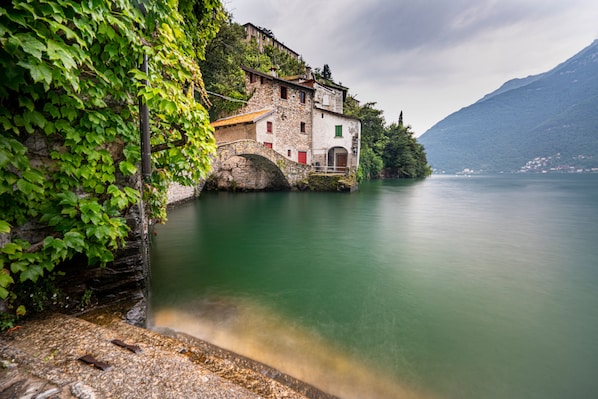 A stone building with a bridge, a calm lake, and a mountain in the background.