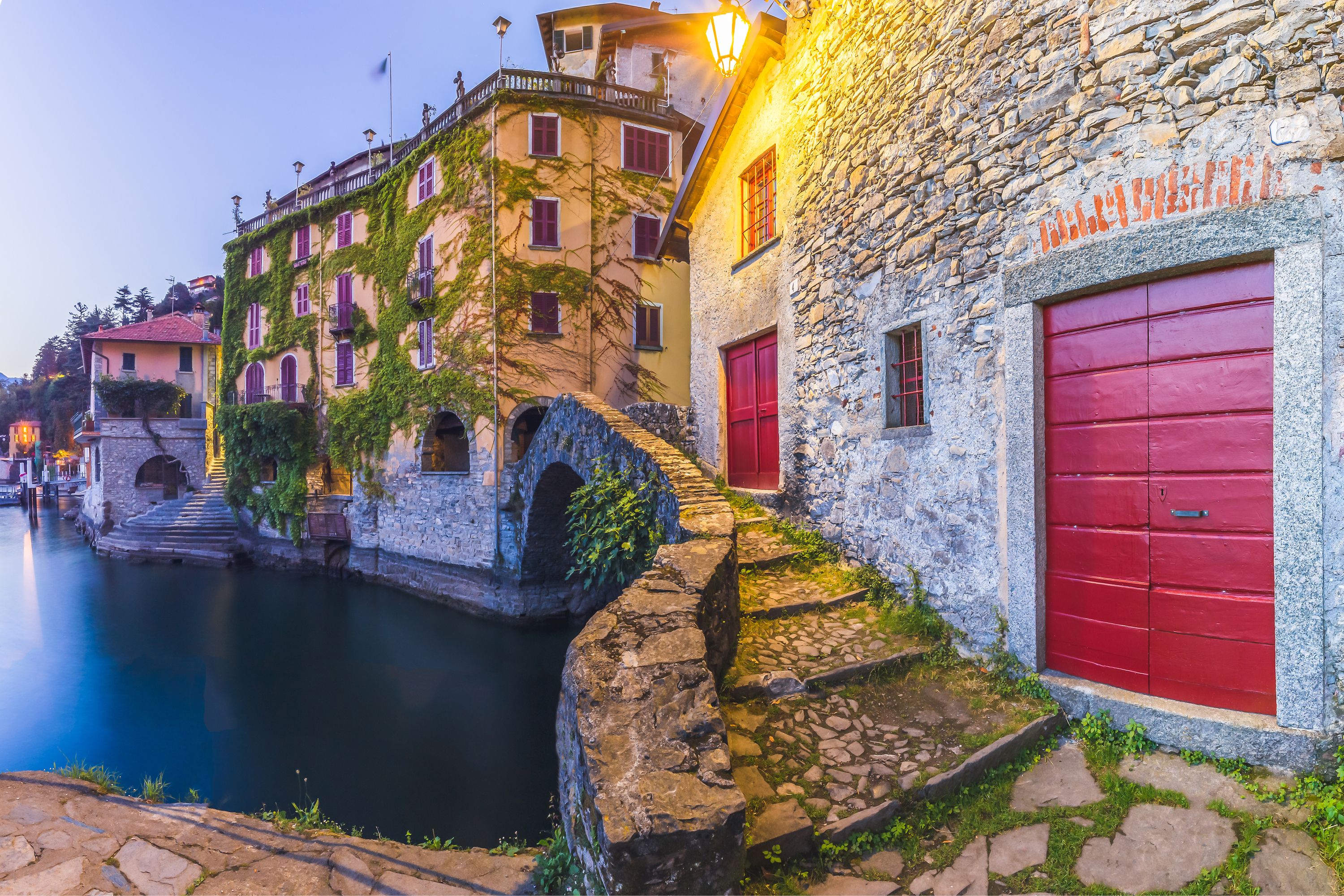 A stone building with a red door and a stone bridge over a canal.