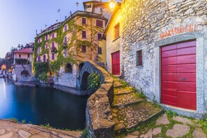 A stone building with a red door and a stone bridge over a canal. - Villa Marilyn (Nesso)