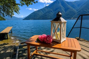 A wooden table with a lantern and flowers by a lake with mountains in the background. - Villa Marilyn (Nesso)
