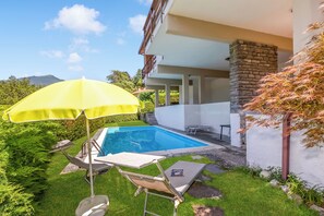 Una piscina con una sombrilla amarilla, una silla de descanso y un muro de piedra.