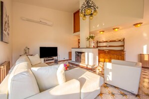 Una sala de estar con sofá, televisión, chimenea y una cocina al fondo.