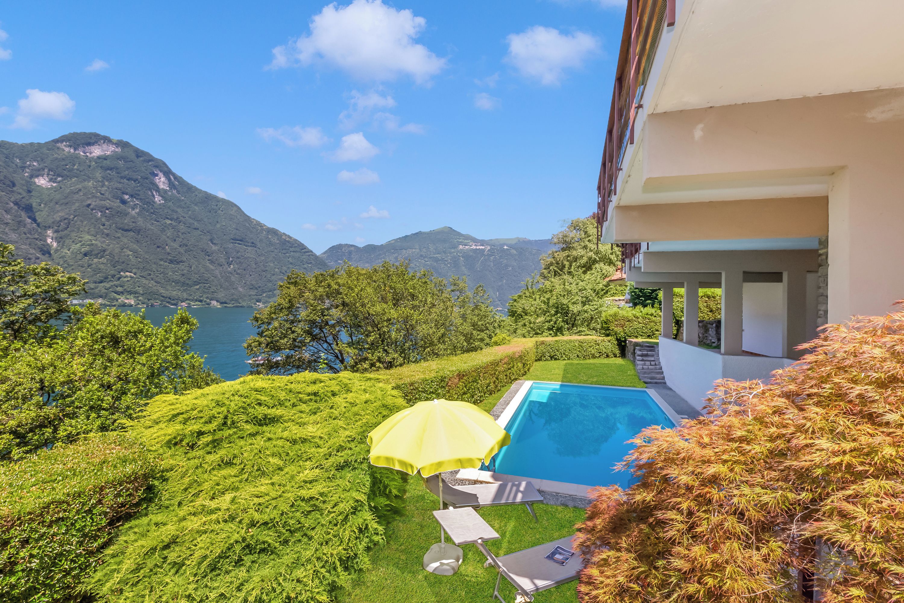 A pool with a yellow umbrella, surrounded by lush greenery and mountains in the background.
