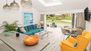 A modern living room with a teal sofa, a yellow armchair, and a dining area with a glass table. - Summerhouse (Tenby)