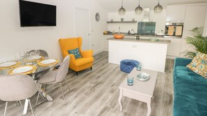 A modern living room with a dining area, a kitchen, and a TV mounted on the wall. - Summerhouse (Tenby)
