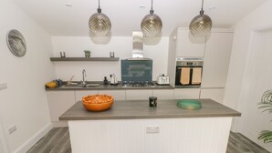 A modern kitchen with a central island, white cabinetry, and pendant lighting. - Summerhouse (Tenby)