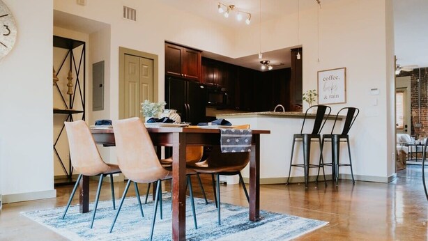 A modern kitchen with dark cabinets, a central island, and a dining area with a table and chairs. - Stunning townhouse on quiet street in Springfield! (Jacksonville)