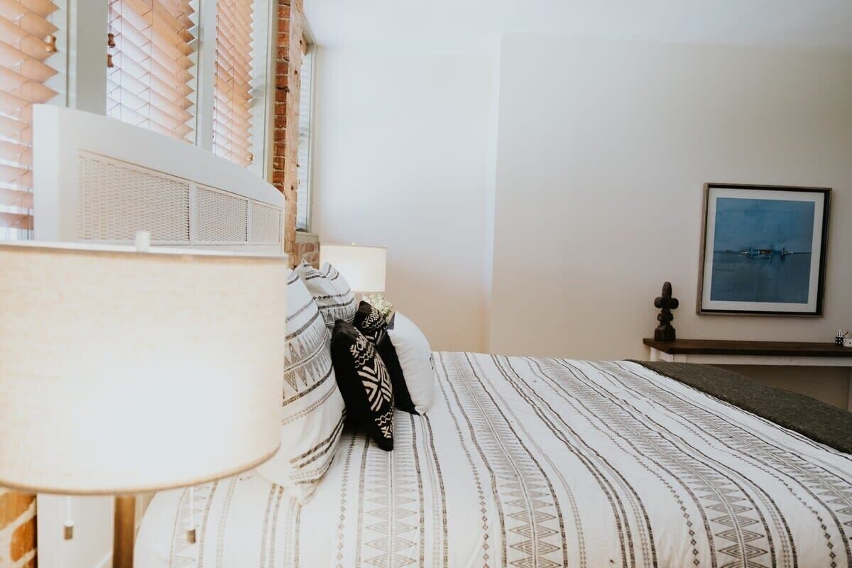 A bedroom with a bed, a lamp, a picture on the wall, and a window with blinds.