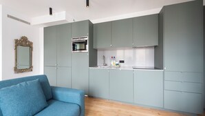 A modern kitchen with grey cabinets, a built-in oven, and a blue sofa in a living area. - Childe Harold, 4 stars, Luxurious and close to the Arc de Triomphe (París)