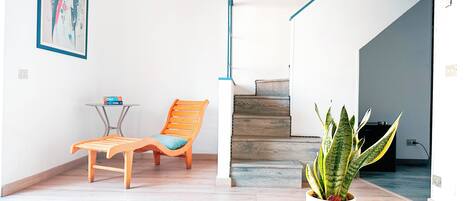 Un interior moderno con una silla de madera, una mesita, una planta en maceta y una escalera.