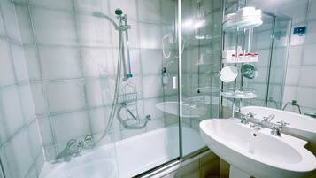 Een moderne badkamer met een douche met glazen wand, een witte badkuip en een wastafel met spiegel erboven.