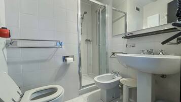 A modern bathroom with white tiles, a glass shower enclosure, a bidet, a toilet, and a sink with a mirror above.