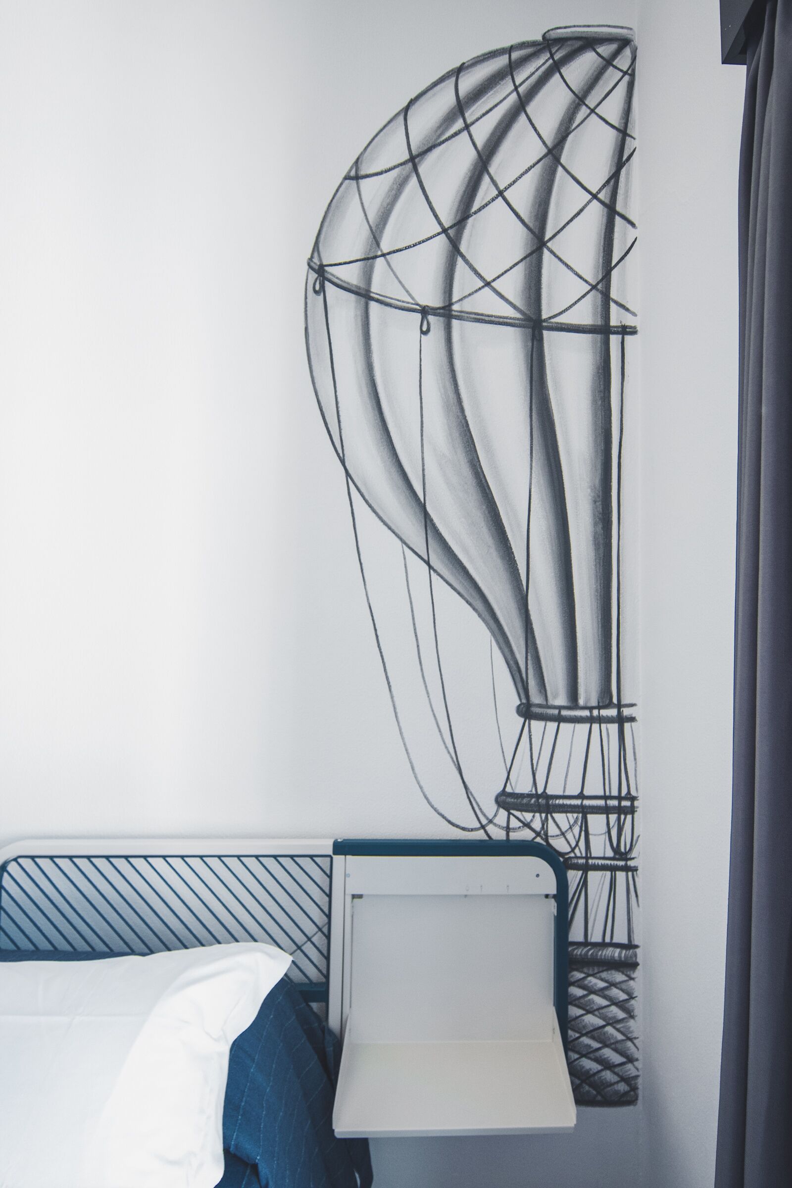Un lit avec une tête de lit bleue et un oreiller blanc, une table de chevet avec un plateau blanc, et une œuvre d’art abstraite accrochée au mur.
