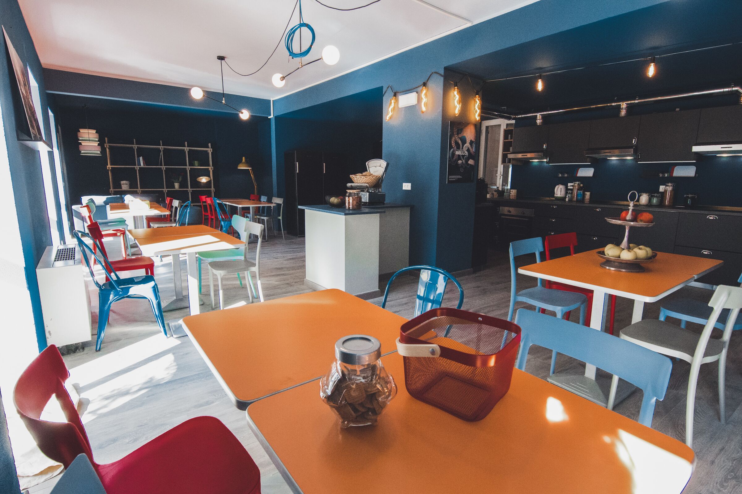 Ein modernes Restaurant mit orangefarbenen Tischen und blauen Stühlen, einem Küchenbereich und einer Bar.
