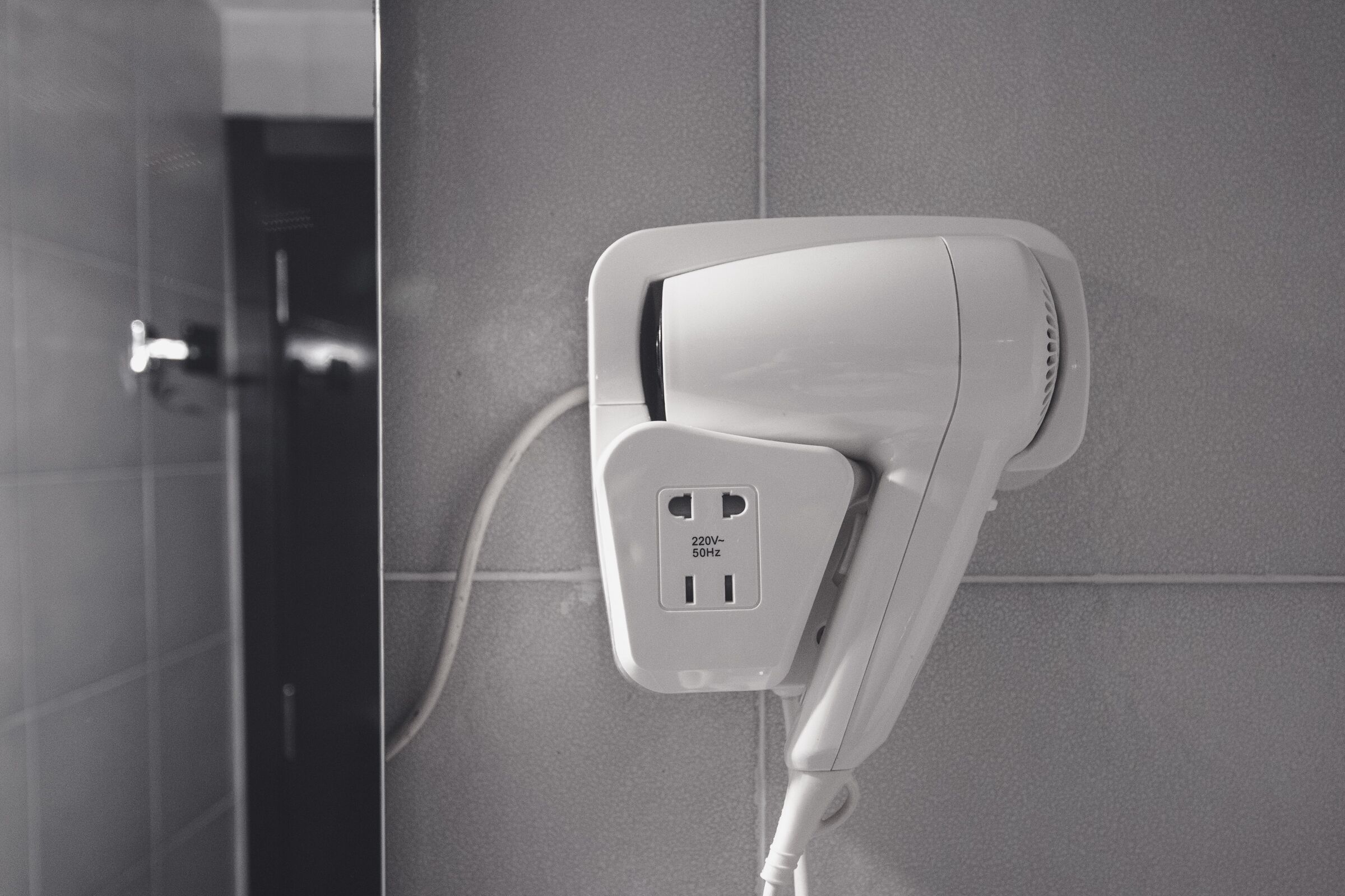 A hairdryer mounted on a tiled wall with a power outlet.
