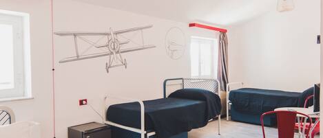 A dormitory room with bunk beds, a desk, and a chair. There is a window, a radiator, and a wall-mounted lamp.