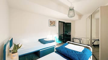 Ein Schlafzimmer mit einem Bett, einem kleinen Tisch, einem Stuhl, einer Topfpflanze und einer Pendelleuchte.