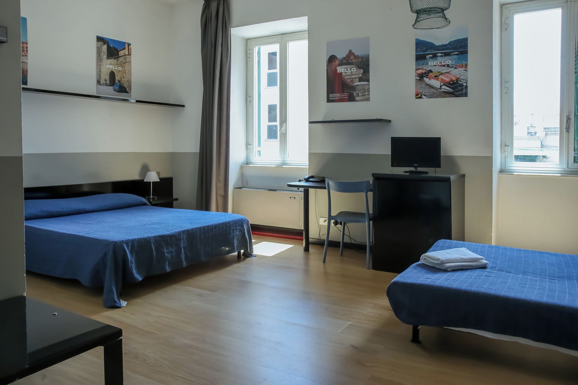A hotel room with two beds, a desk, a chair, a television, and a window.