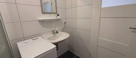 A small bathroom with a white sink, mirror, and a white washing machine.