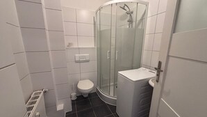 A compact bathroom with a glass-enclosed shower, a toilet, and a washing machine.